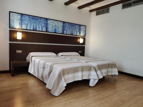 A cozy hotel room features a neatly made bed with striped bedding, wooden floors, exposed beams, and blue artwork above the headboard, ideal for travelers seeking comfort and simplicity.