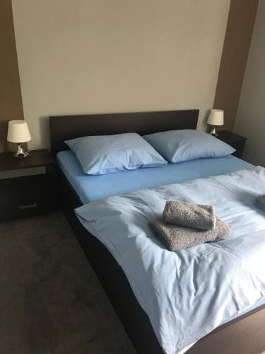 A cozy hotel room features a neatly made bed with blue linens, two bedside tables with lamps, and a folded towel, ideal for travelers seeking comfort and simplicity.