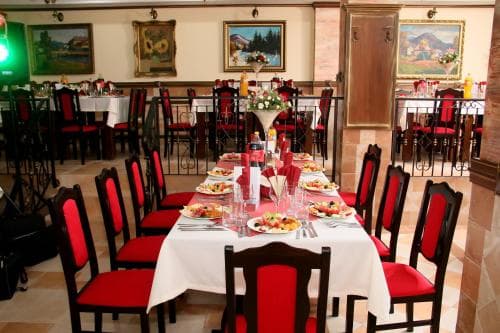 A cozy restaurant with red chairs and white tablecloths set for dining, adorned with wall paintings and warm lighting, ideal for travelers seeking an intimate dining experience.