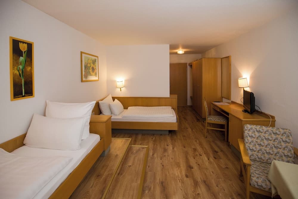 A cozy hotel room with wooden flooring, neatly arranged twin beds, floral artwork, and a warm ambiance is ideal for travelers seeking comfort and simplicity.