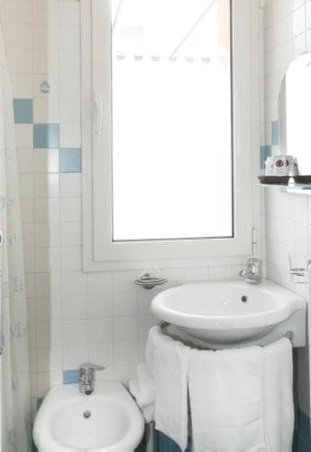 A bright, clean bathroom with white tiled walls, dual sinks, neatly folded towels, and a window letting in natural light, ideal for travelers seeking a cozy and functional accommodation space.
