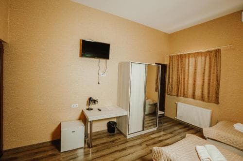 A cozy hotel room features warm-toned walls, a neatly made bed, a desk with a chair, a wardrobe, and a mounted TV, ideal for travelers seeking comfort and functionality in a budget-friendly accommodation.