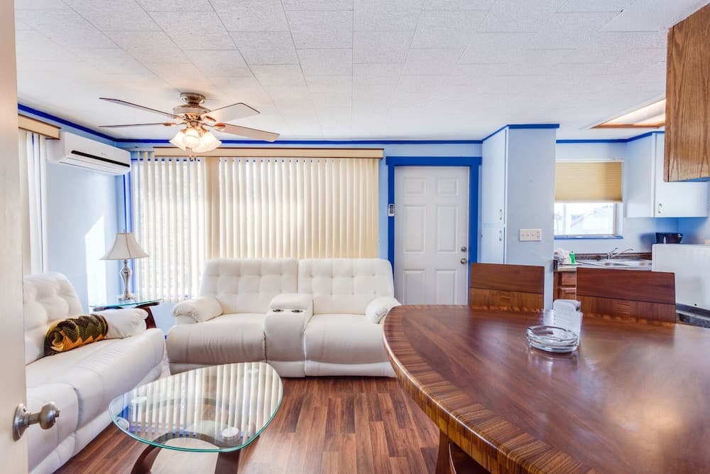 A cozy apartment living space features white tufted sofas, wooden flooring, and blue-trimmed walls, creating a welcoming atmosphere ideal for travelers seeking comfort and functionality.