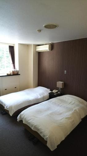 A cozy hotel room with two neatly made beds, a window with curtains, and simple decor offers a comfortable stay for travelers seeking rest in a quiet urban setting.