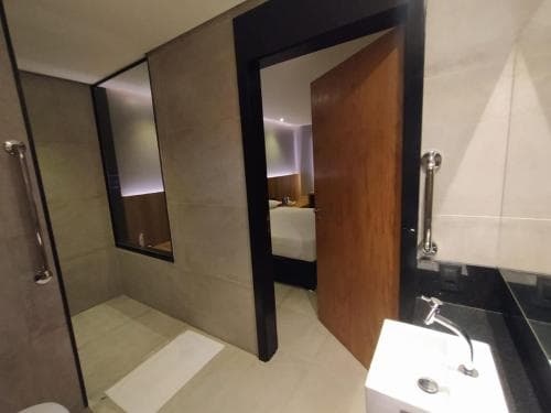 A modern bathroom with sleek tiled walls, a glass shower enclosure, and a wooden door leading to a cozy bedroom creates an inviting atmosphere, ideal for travelers seeking comfort and style in their accommodations.