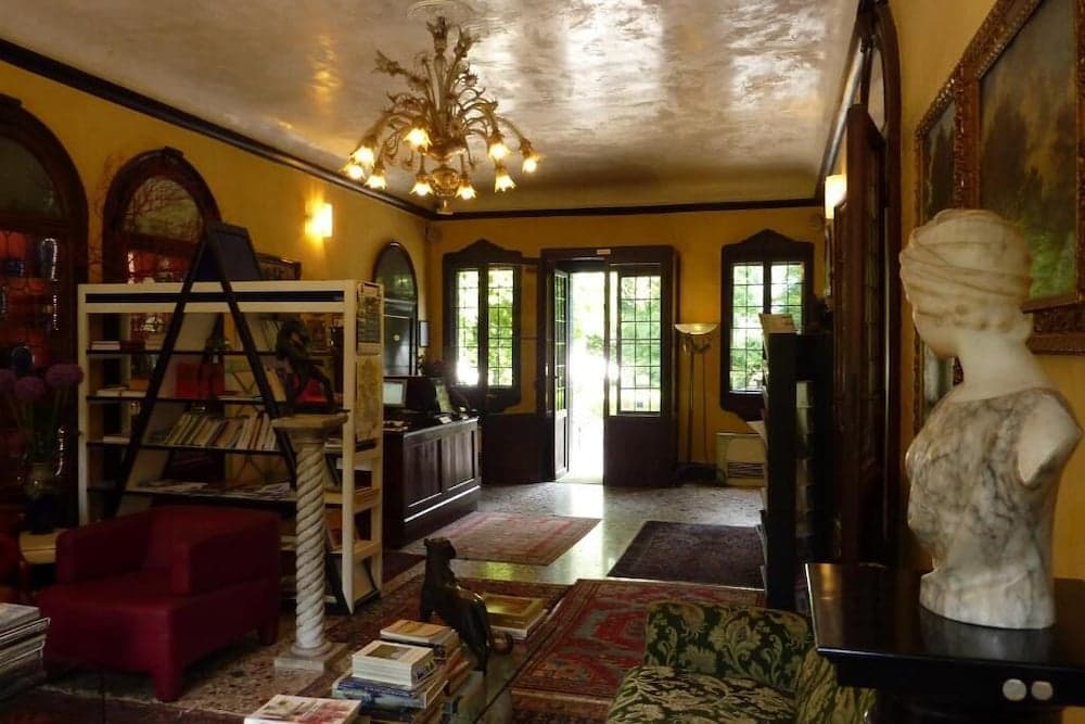 A cozy, warmly lit indoor space features ornate yellow walls, a chandelier, antique furniture, and artistic decor, creating an inviting atmosphere ideal for a boutique hotel or cultural retreat.