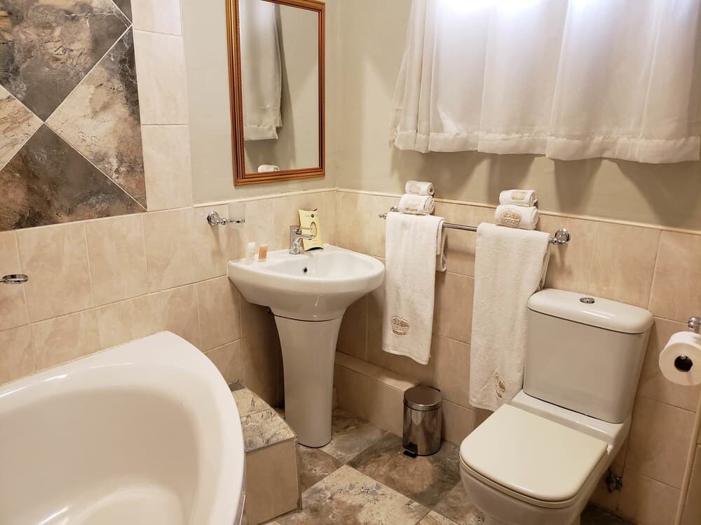 A cozy hotel bathroom features a bathtub, sink, toilet, neatly arranged towels, and a framed mirror, creating a warm and inviting atmosphere ideal for travelers seeking comfort and cleanliness.
