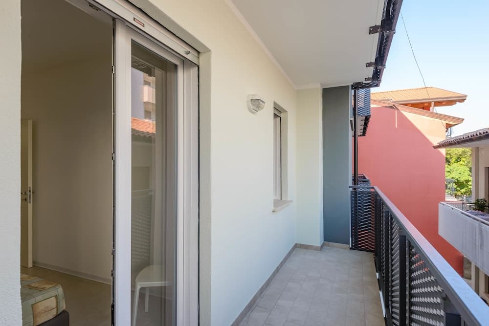 A serene balcony with tiled flooring, modern sliding glass doors, and a view of vibrant red walls and greenery, ideal for travelers seeking a cozy retreat in an urban apartment setting.