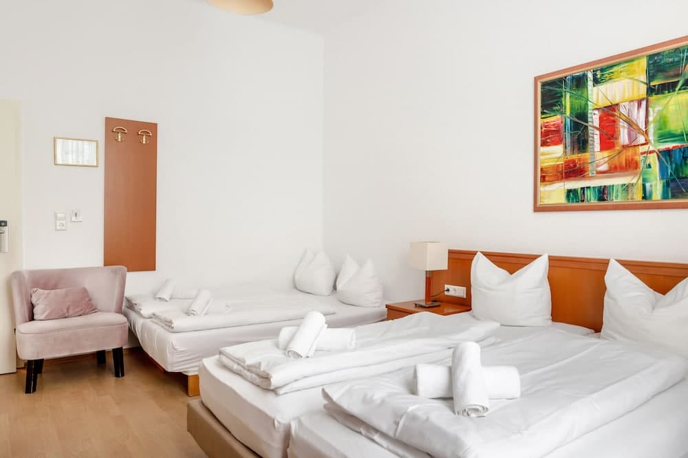 A cozy hotel room features neatly arranged twin beds with white linens, a soft pink armchair, vibrant abstract wall art, and warm wooden accents, ideal for travelers seeking comfort and relaxation.