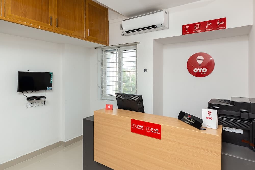 A clean and organized hotel reception area features a wooden desk with an OYO Rooms logo, a computer setup, and a wall-mounted TV, ideal for travelers seeking efficient check-in services in a professional environment.