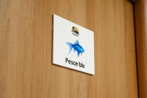 A serene hotel room door features a sign with a blue fish graphic labeled "Pesce blu," ideal for travelers seeking a themed accommodation experience.