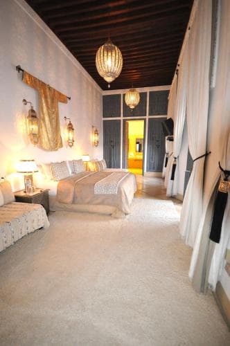 A cozy, warmly lit hotel suite features plush bedding, elegant curtains, and ornate lanterns, creating an inviting atmosphere ideal for travelers seeking comfort and luxury.