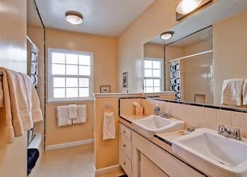 A cozy bathroom with dual sinks, a large mirror, soft yellow walls, and neatly hung towels creates a serene atmosphere ideal for travelers seeking comfort and cleanliness during their stay.