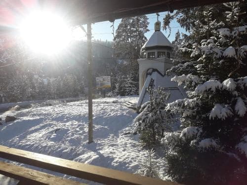 A serene winter scene captures a snow-covered landscape with evergreen trees, a small church dome, and bright sunlight, ideal for a peaceful ski resort getaway.
