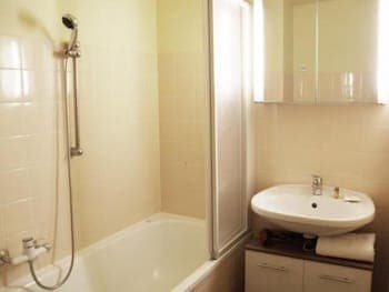 A cozy, well-lit bathroom featuring a bathtub with a shower attachment, a sink with a mirrored cabinet, and soft yellow tiles, ideal for travelers seeking comfort in compact accommodations.