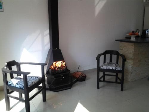 A cozy indoor setting features two cushioned chairs flanking a warm wood-burning stove, creating an inviting atmosphere ideal for relaxation in a cabin or retreat space.