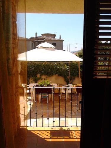 A serene courtyard view framed by an open doorway, featuring a tiled patio, white umbrella, and lush greenery, evokes a tranquil vacation retreat perfect for relaxation.