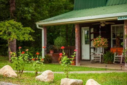 A serene countryside retreat features a cozy porch adorned with vibrant flowers and rocking chairs, surrounded by lush greenery, ideal for a peaceful getaway.