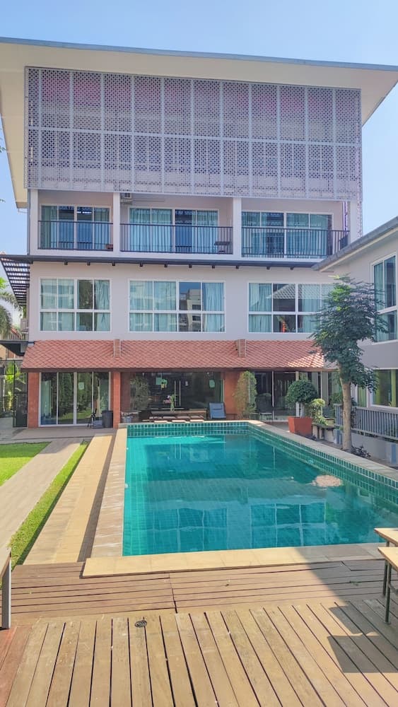 A serene tropical resort features a sparkling pool surrounded by lush greenery and a modern building with balconies, ideal for vacationers seeking relaxation and comfort.
