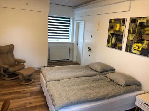 A cozy bedroom with twin beds, modern artwork, and a comfortable armchair by the window, ideal for travelers seeking a quiet and stylish accommodation.