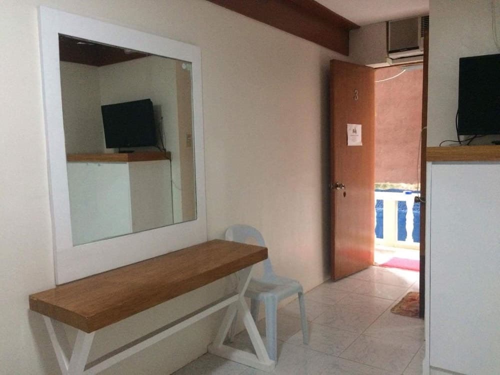 A cozy hotel room entrance features a wooden bench, mirror, plastic chair, tiled floor, and a door leading to a balcony, ideal for travelers seeking a simple and functional accommodation space.