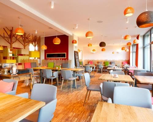 A vibrant indoor café with colorful pendant lights, modern furniture, and a warm ambiance offers an inviting space for travelers seeking a cozy dining or meeting spot.