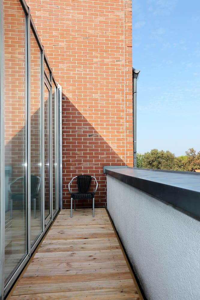 A serene balcony with wooden flooring, a lone chair, and a brick wall backdrop offers a tranquil retreat, perfect for travelers seeking relaxation amidst urban settings.
