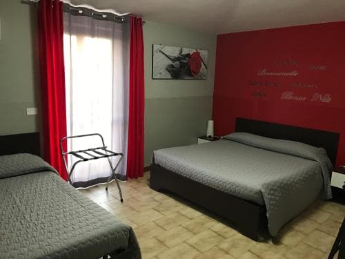 A cozy hotel room features two neatly made beds, vibrant red curtains, and a patterned floor, creating a welcoming atmosphere ideal for travelers seeking comfort and relaxation.