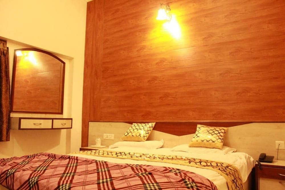 A cozy hotel room features a neatly made bed with patterned bedding against a warm wooden accent wall, complemented by soft lighting and a mirrored vanity, ideal for travelers seeking comfort and relaxation.