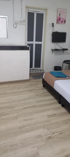 A cozy hotel room with wooden flooring, a neatly made bed, a small desk area, and a mounted TV creates a welcoming atmosphere ideal for travelers seeking comfort and simplicity.