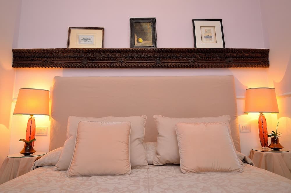A cozy bedroom with a plush bed adorned with beige pillows, flanked by warm-lit lamps and framed artwork above, ideal for travelers seeking comfort and relaxation.