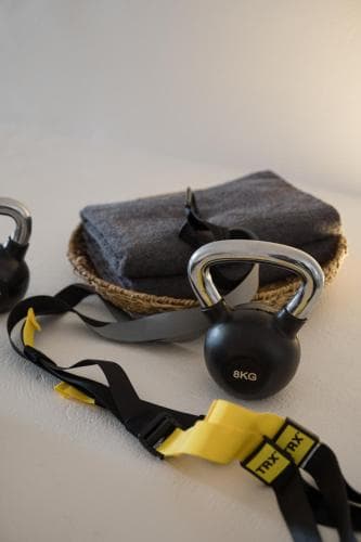 A cozy indoor workout setup featuring kettlebells, TRX straps, and a towel in a woven basket, ideal for home fitness enthusiasts seeking a compact and versatile training space.