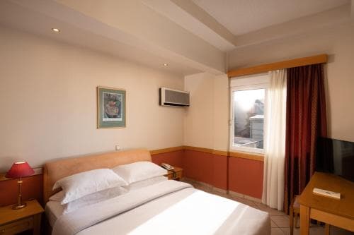 A cozy hotel room with a neatly made bed, wooden furniture, and a window draped with curtains offers a comfortable stay for travelers seeking relaxation.