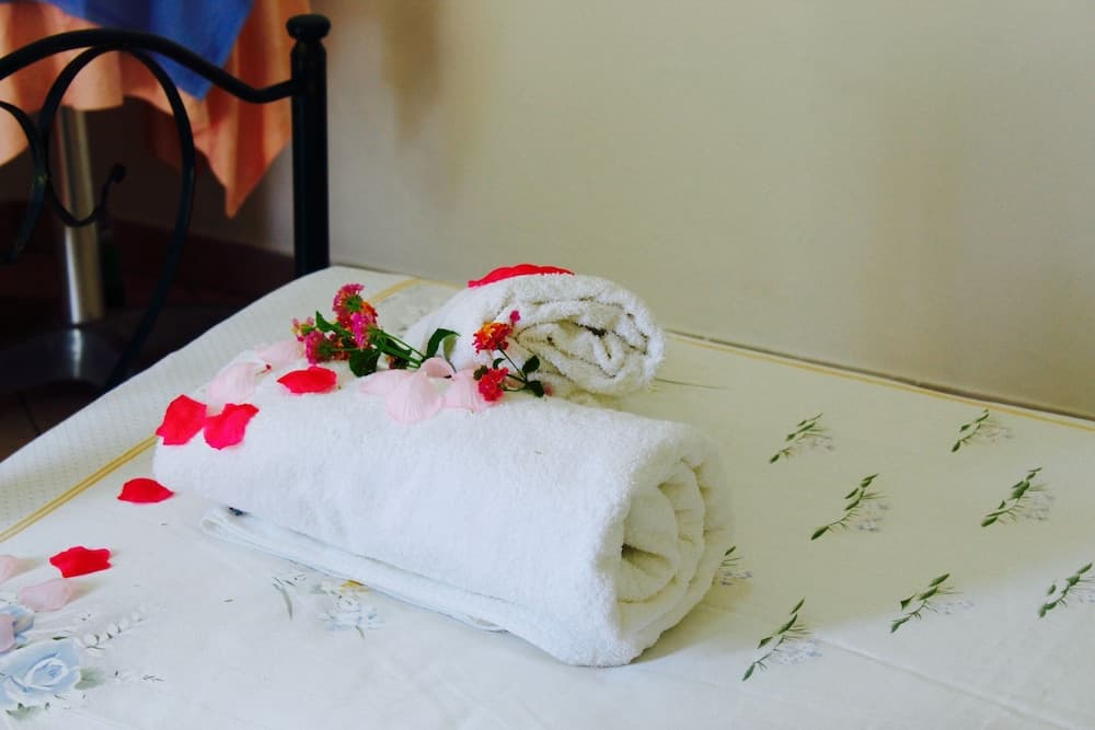 A cozy hotel room scene features neatly rolled white towels adorned with vibrant flower petals on a floral-patterned bedspread, evoking a romantic and inviting atmosphere ideal for honeymoon travelers.