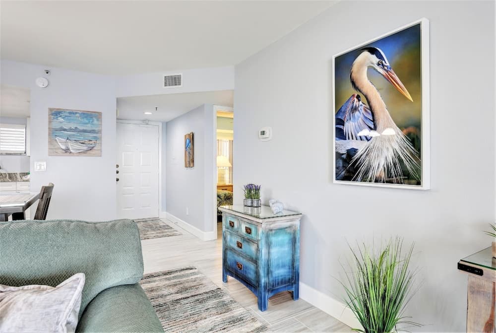A serene coastal-themed living space features a vibrant heron painting, a blue distressed dresser, and nautical decor, ideal for a relaxing beachside vacation rental.