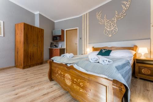 A cozy hotel room features a wooden bed adorned with a geometric deer wall art, warm lighting, and neatly arranged towels, ideal for travelers seeking comfort and charm.