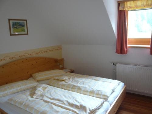 A cozy bedroom with a wooden bed, striped bedding, and a window with red curtains offers a serene retreat for travelers seeking a peaceful accommodation experience.