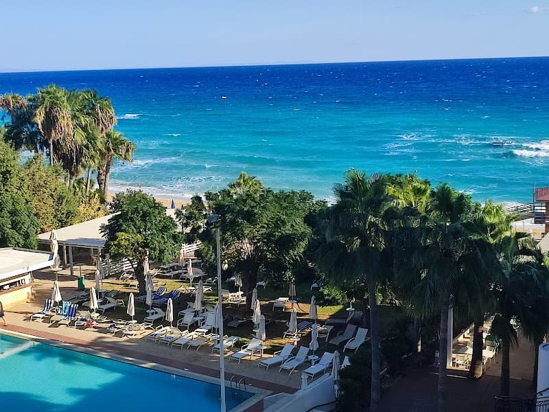 A serene beachfront resort scene features a sparkling pool lined with lounge chairs under palm trees, overlooking the vibrant turquoise sea, ideal for a relaxing vacation getaway.