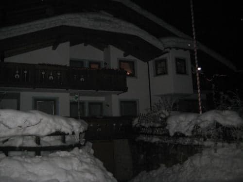 A cozy, snow-covered chalet at night exudes a serene winter ambiance, perfect for travelers seeking a peaceful mountain retreat with its illuminated windows and snow-laden balconies.