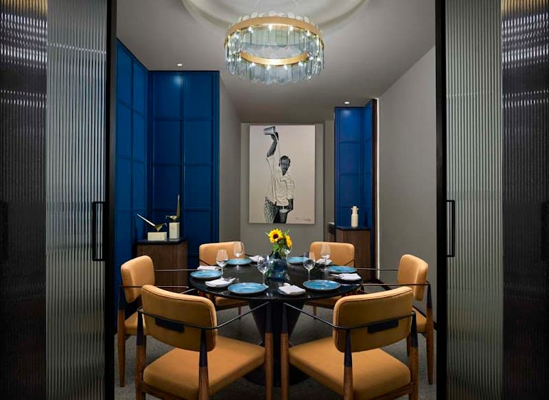 A luxurious dining room at Hyatt Centric Hebbal Bengaluru features modern decor with blue walls, a crystal chandelier, and a vibrant centerpiece, ideal for travelers seeking upscale accommodations in a sophisticated setting.