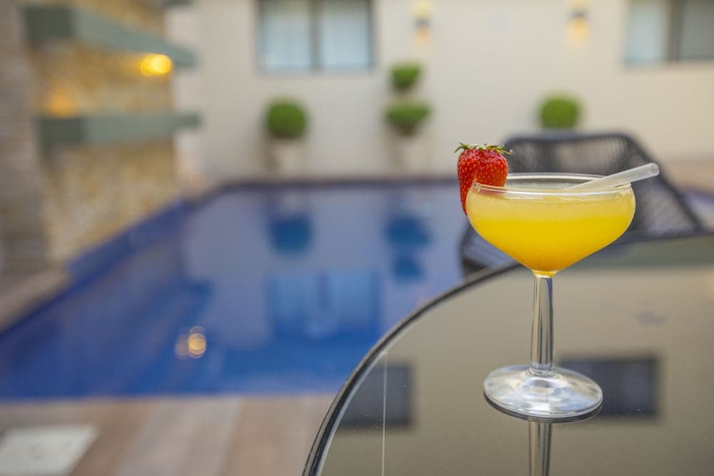 A vibrant yellow cocktail garnished with a strawberry sits on a glass table by a serene poolside setting, evoking a relaxing vacation atmosphere perfect for leisure travelers seeking tranquility.