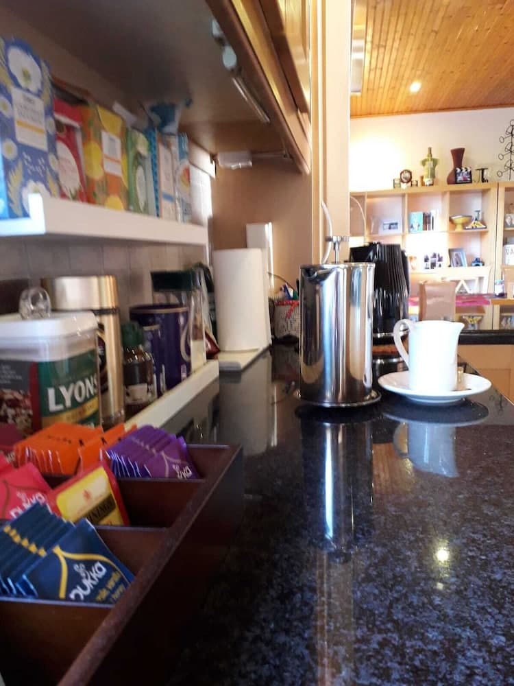 A cozy café corner features a polished countertop with a steaming coffee pot, neatly arranged tea bags, and shelves stocked with colorful boxes, creating an inviting atmosphere perfect for travelers seeking a warm beverage stop.