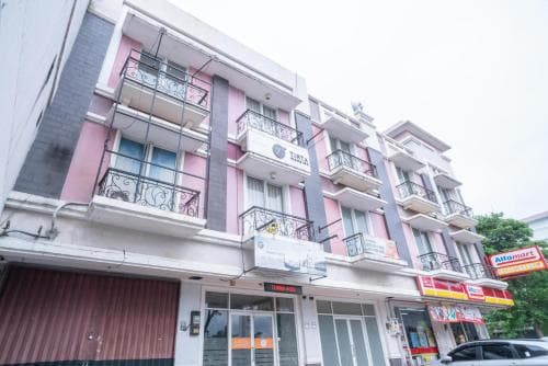 A vibrant pink and gray apartment building with balconies and storefronts below offers a cozy urban retreat, ideal for travelers seeking a local experience in a bustling city neighborhood.