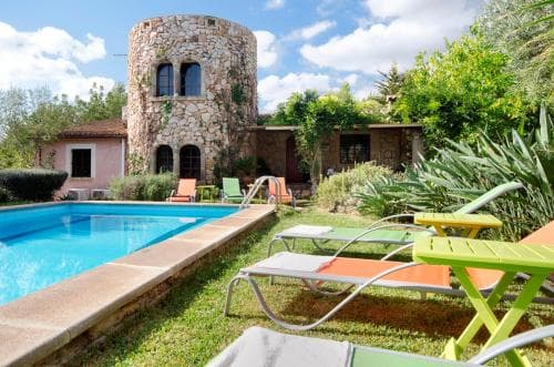 A serene countryside retreat features a charming stone tower villa with a vibrant poolside area, surrounded by lush greenery, ideal for relaxing vacations.