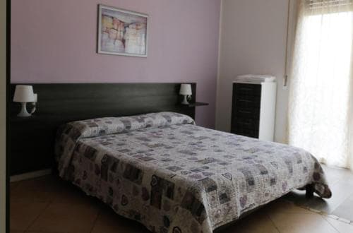 A cozy hotel room features a neatly made bed with patterned bedding, soft purple walls adorned with abstract art, and ambient lighting from bedside lamps, ideal for travelers seeking comfort and relaxation.