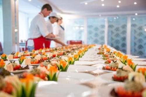 A vibrant banquet hall features an elegant spread of colorful appetizers on long tables, with chefs in the background, ideal for corporate events or luxury dining experiences.