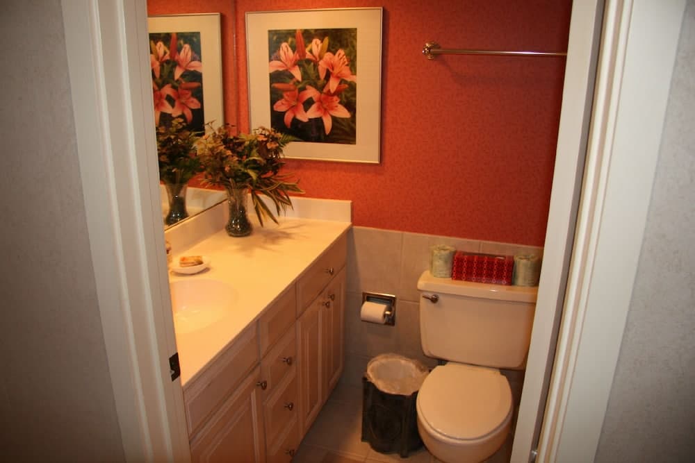 A cozy bathroom with warm red walls, floral artwork, and a neatly arranged vanity offers a serene retreat for travelers seeking comfort and style.