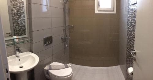 A modern bathroom with sleek tiled walls, a compact shower area, and a sink with a mirror, ideal for travelers seeking clean and efficient accommodations.