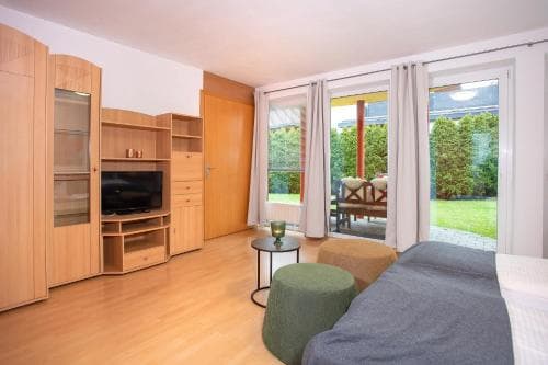 A cozy bedroom with wooden furniture, a flat-screen TV, and a sliding glass door leading to a lush garden, ideal for travelers seeking comfort and relaxation in a serene setting.