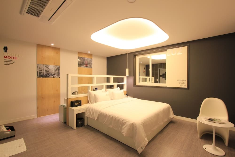 A cozy motel room features a neatly made bed under a modern ceiling light, complemented by stylish decor and a minimalist chair, ideal for travelers seeking comfort and design in their accommodations.